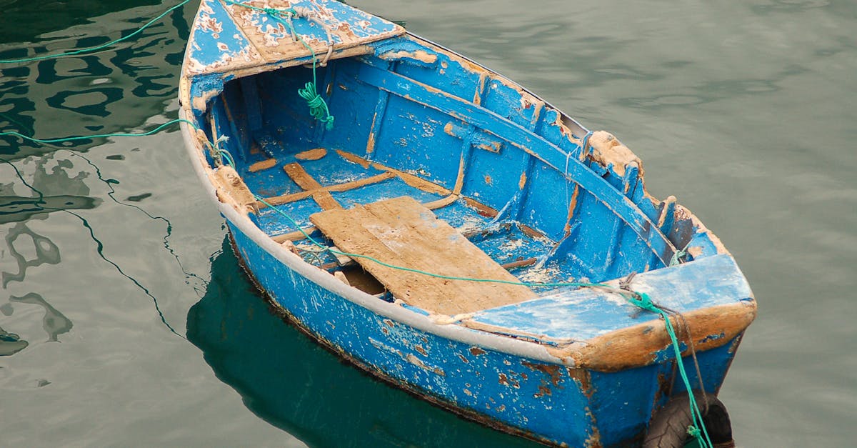 A dilapidated blue rowboat with rope, floating in calm water, showcasing rustic charm.