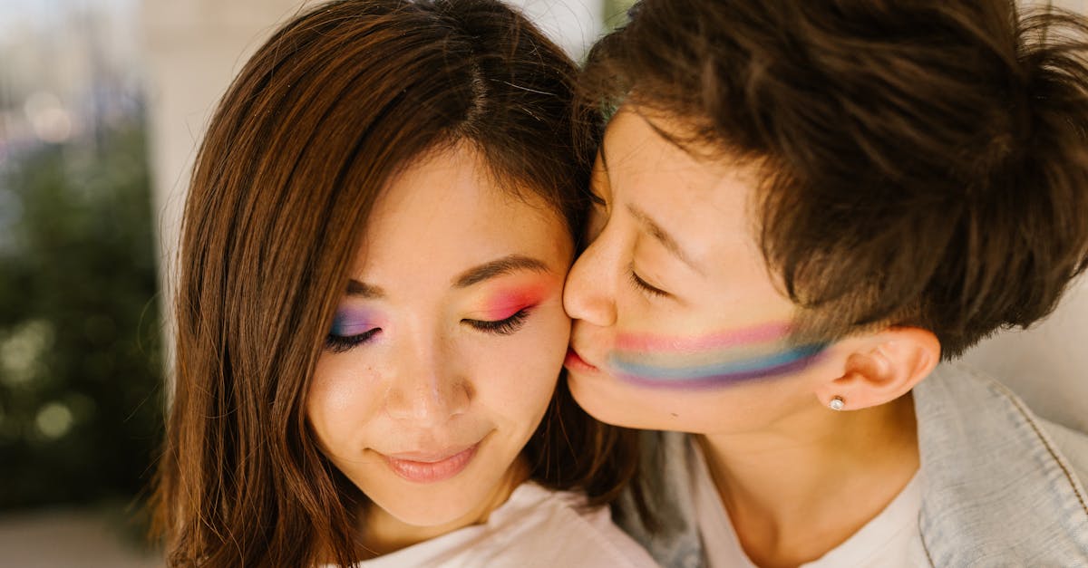 Close-up portrait of two women, one kissing the other on the cheek, both with colorful makeup.