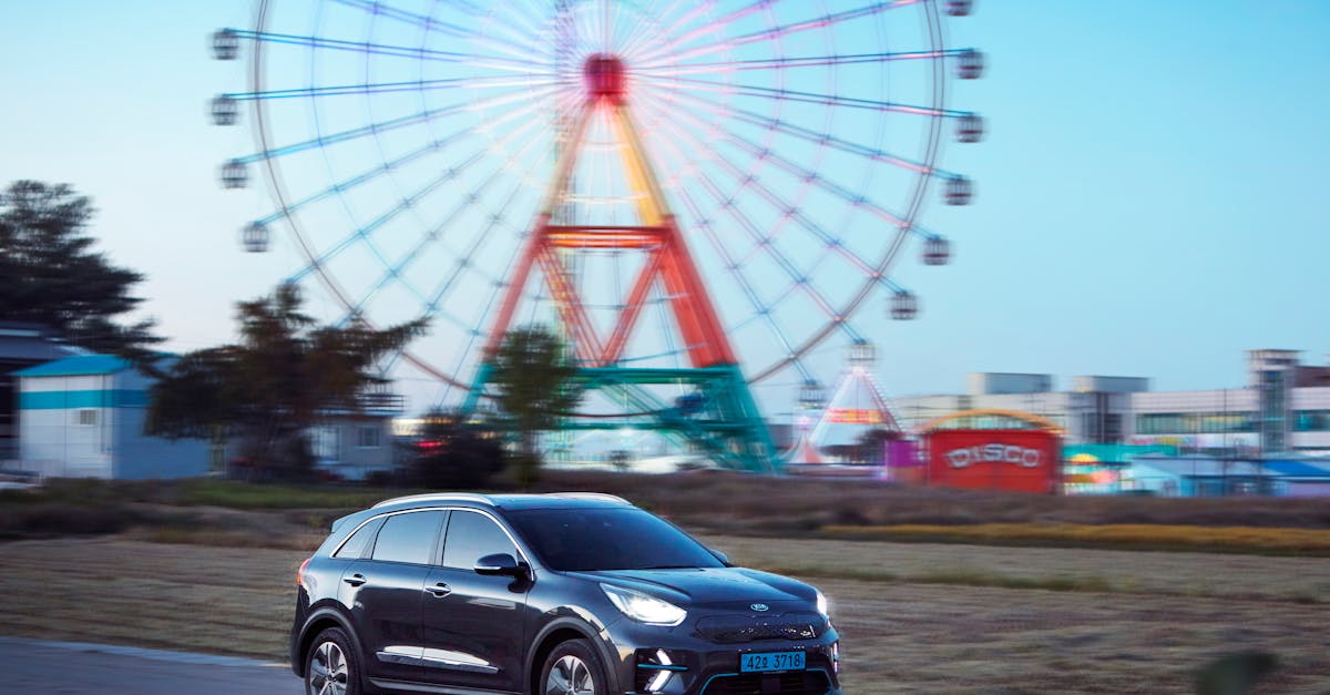 Electric SUV passes brightly lit Ferris wheel at amusement park.