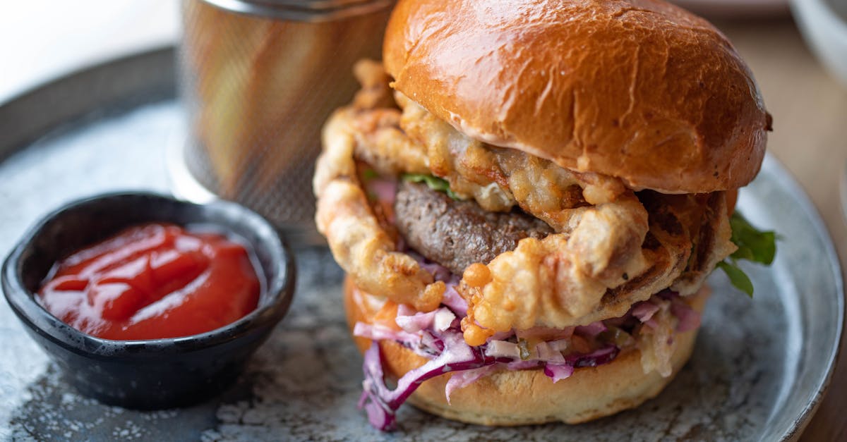 Delicious gourmet burger with crispy onion rings, served with fries and ketchup on a rustic plate.