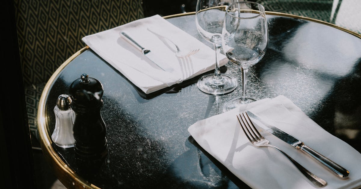 Elegant table setting with wine glasses, cutlery, and a pepper grinder on a glossy surface.