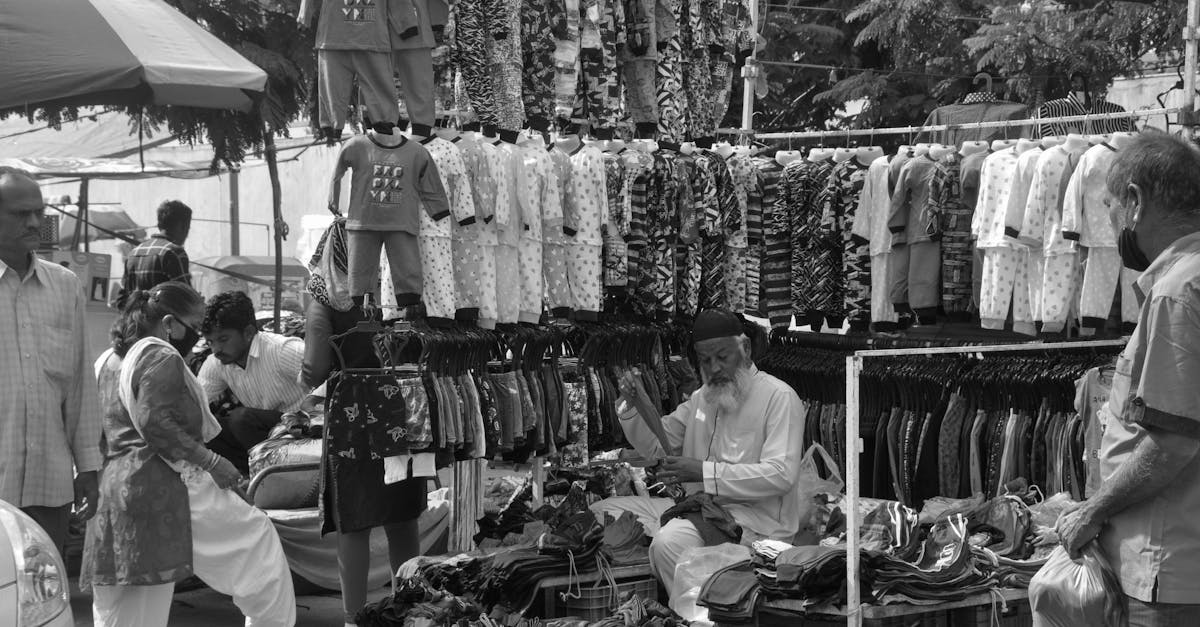Black and white photo of a street vendor selling clothes at an outdoor market.
