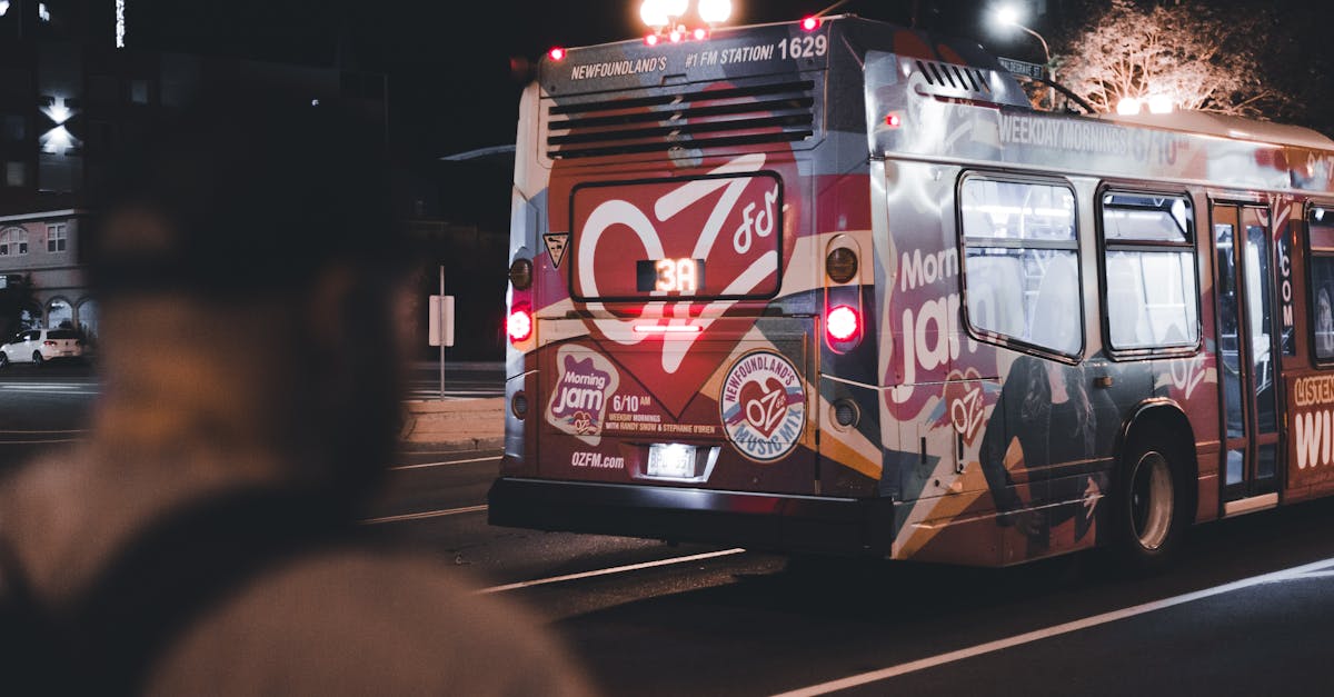 A city bus with colorful advertisements, seen at night with a person in the foreground.