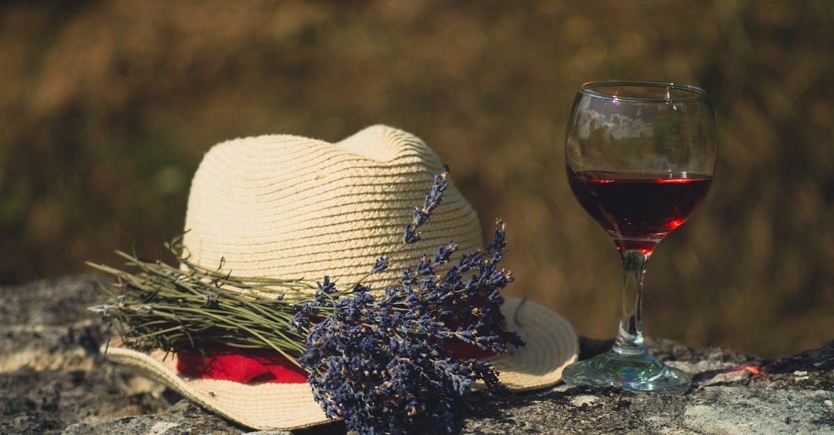 A relaxing outdoor scene with red wine, lavender, and a straw hat on a stone surface.