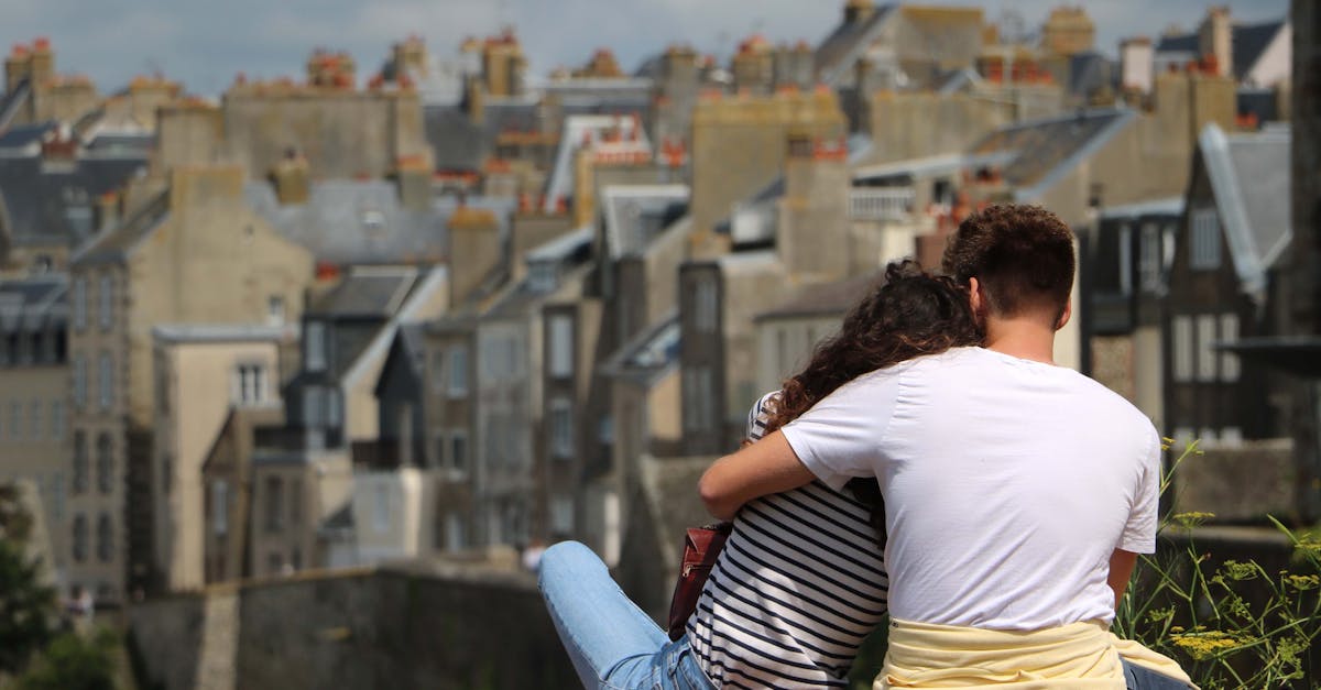 A couple embraces while sitting outdoors overlooking the Granville cityscape in Normandy, France.