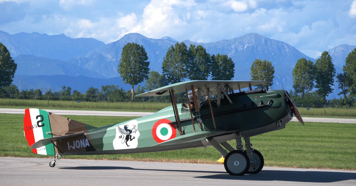 Historic Italian biplane on tarmac set against a scenic mountain backdrop under a clear sky.