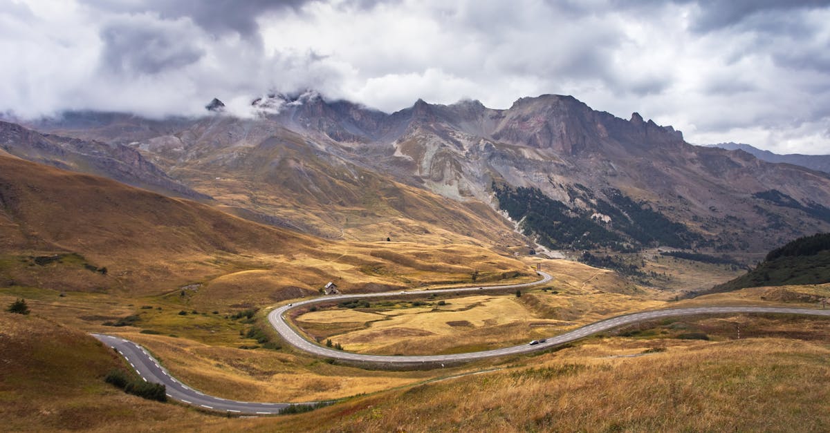 A winding roadway through a mountainous terrain under a dramatic cloudy sky in autumn.
