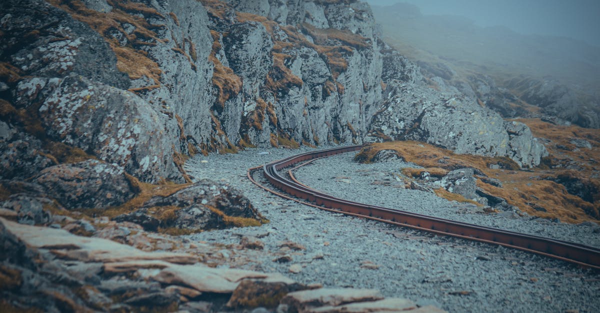 Curved railway track through misty mountains in Wales with scattered rocks and grass.