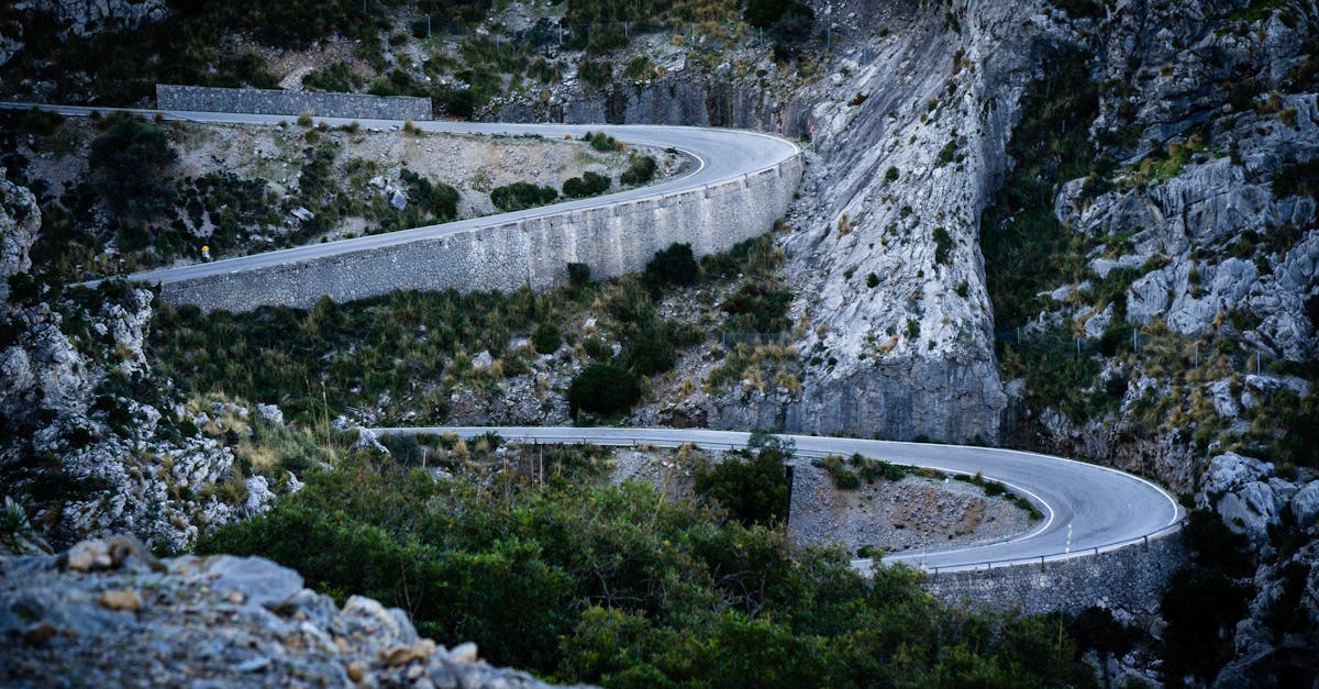 Serpentine mountain road with sharp turns amidst rocky landscape and greenery.