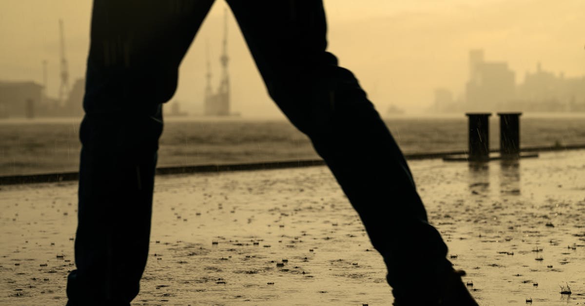 Silhouetted person walking on a rainy urban pavement with raindrops highlighting the wet surface.