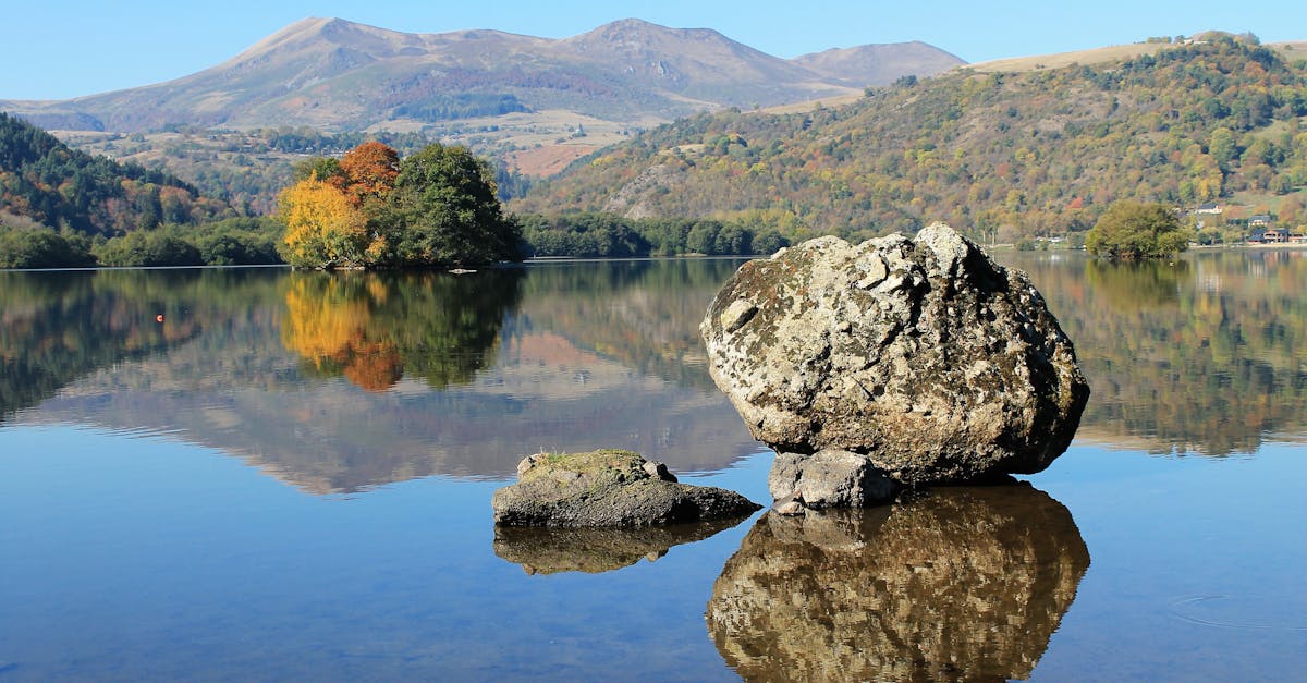 Explore the serene autumn scenery of Chambon Lake with colorful reflections and distant mountains.