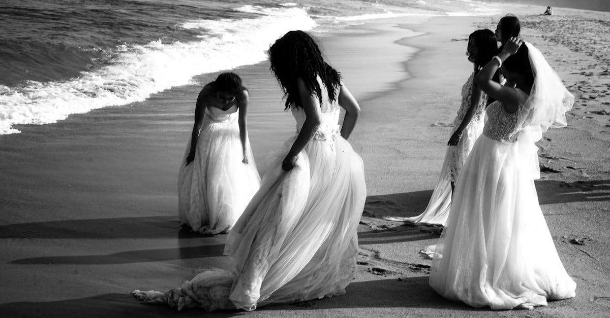 A group of women in wedding dresses gracefully walk along a serene beach shore.