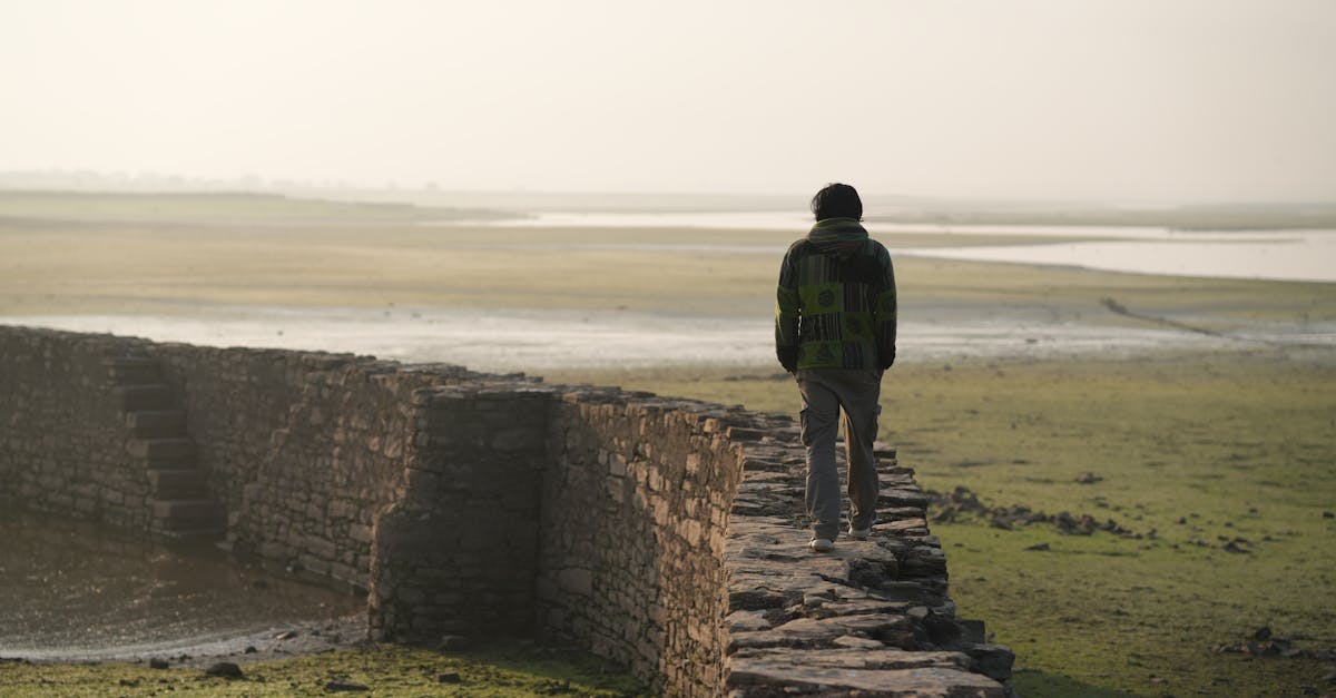 A person walking along a stone wall in a vast, open countryside landscape.