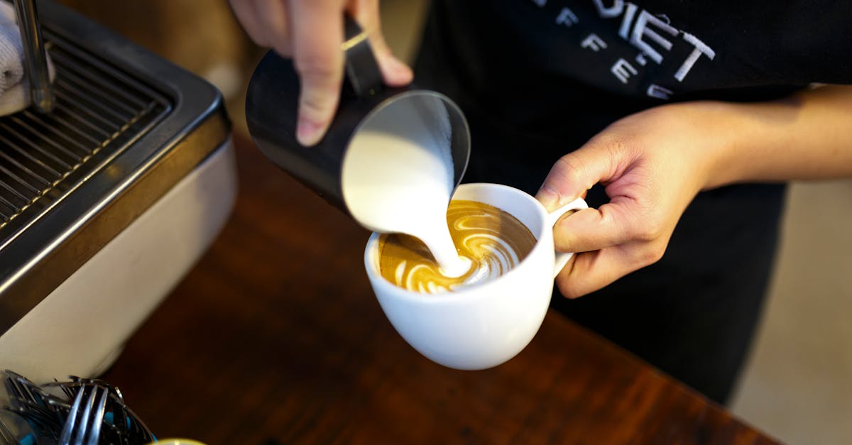 A barista expertly pours milk to create beautiful latte art in a cozy coffee shop setting.