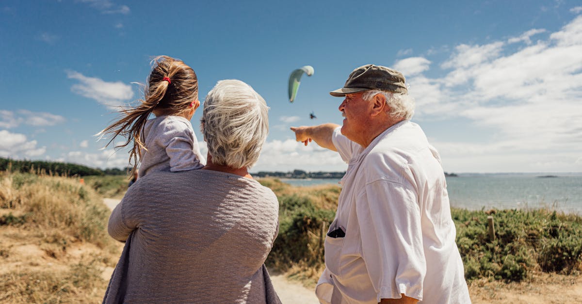 Elderly couple with granddaughter watching the sea and a paraglider on a sunny day in Pénestin, Brittany, France.