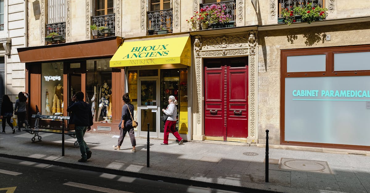 People walking by charming Parisian boutiques on a sunny day, showcasing vintage architecture and lively street life.