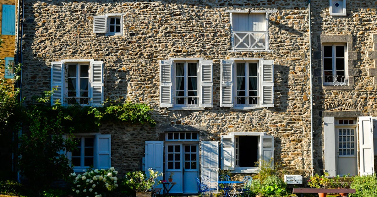 Quaint stone house with blue shutters, sunlight, surrounded by greenery, rich textures.