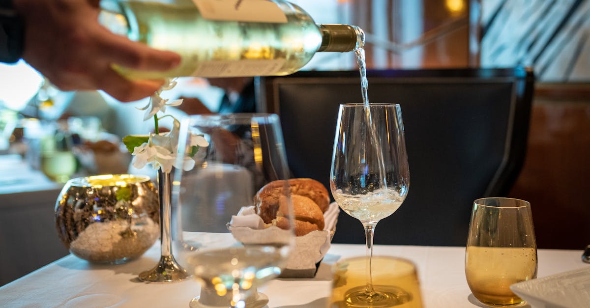 Close-up of wine being poured in a glass on a fine dining table setting.
