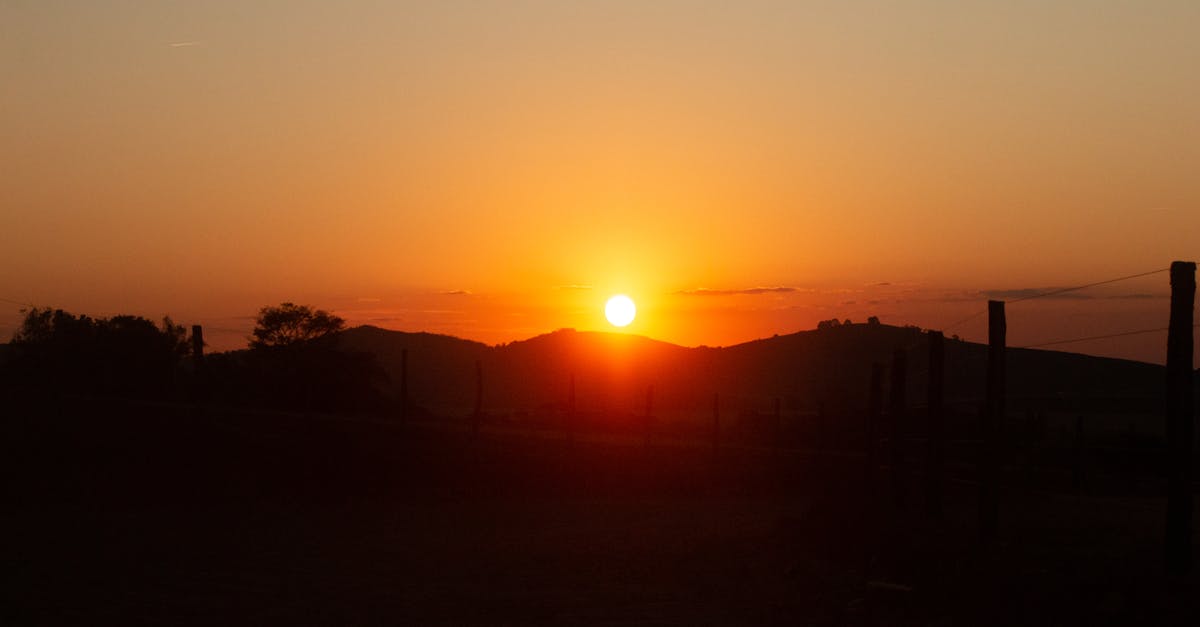 A breathtaking sunset scene with vibrant hues casting over rolling hills and silhouetted trees.