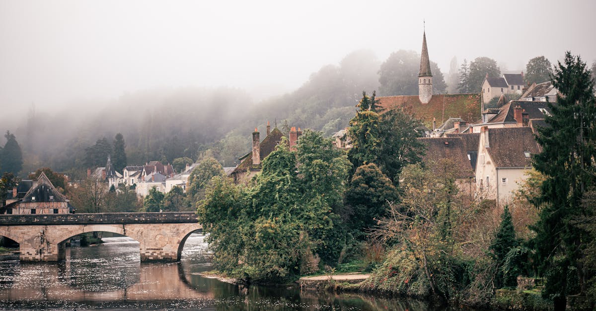 Charming misty morning view of a French village with a historic stone bridge over a river.
