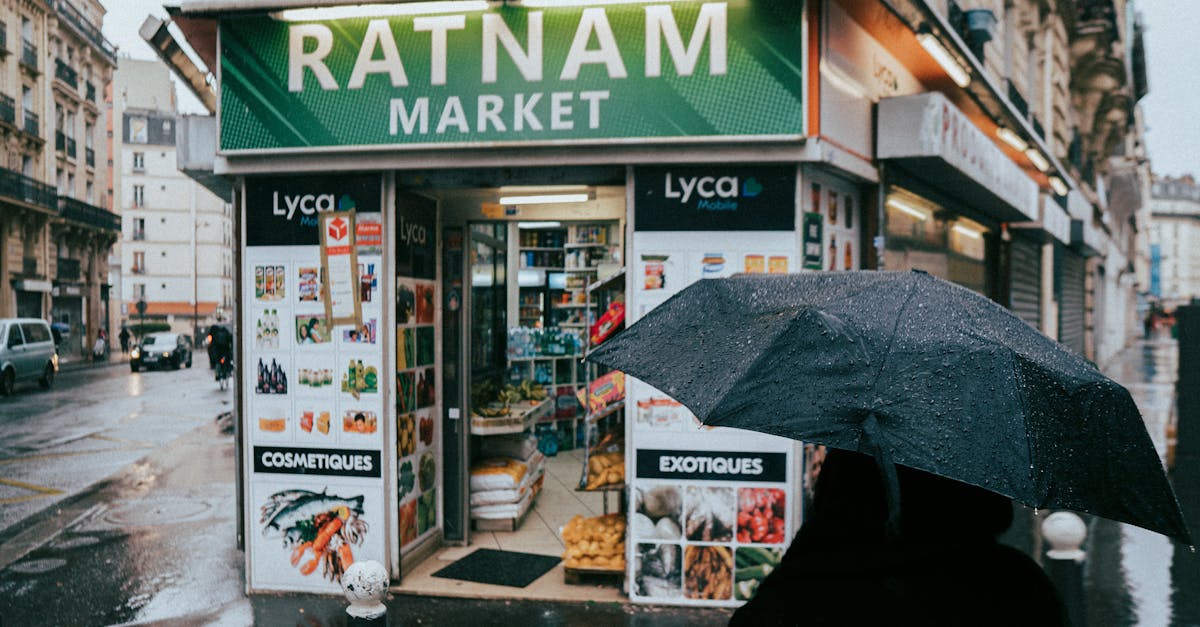 A rainy day in Paris featuring a small corner market with a pedestrian holding a black umbrella.