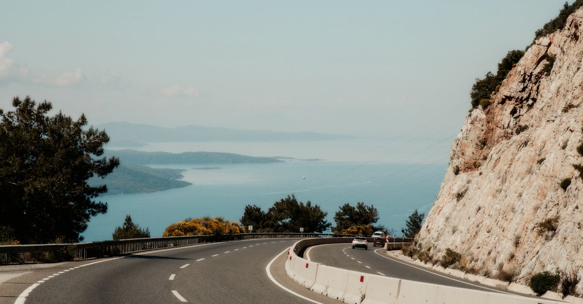 Winding road hugging a rocky cliff with stunning ocean view on a sunny day.