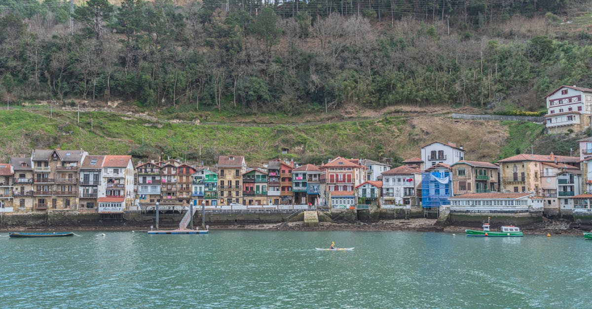 A serene view of colorful houses along a riverbank in the Basque Country, surrounded by lush greenery.