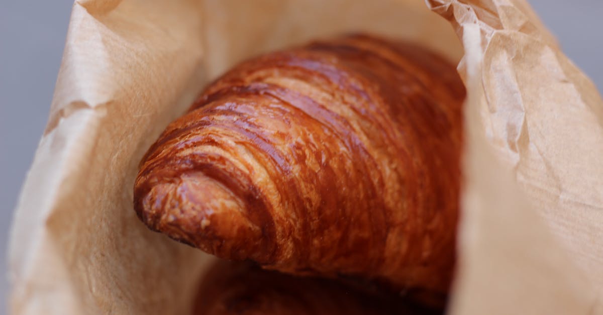 Close-up of a golden croissant inside a brown paper bag, highlighting textured layers.