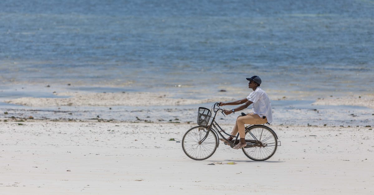 Elegant shot of a man riding a bicycle on a sandy beach with the sea in the background, perfect for travel and lifestyle themes.