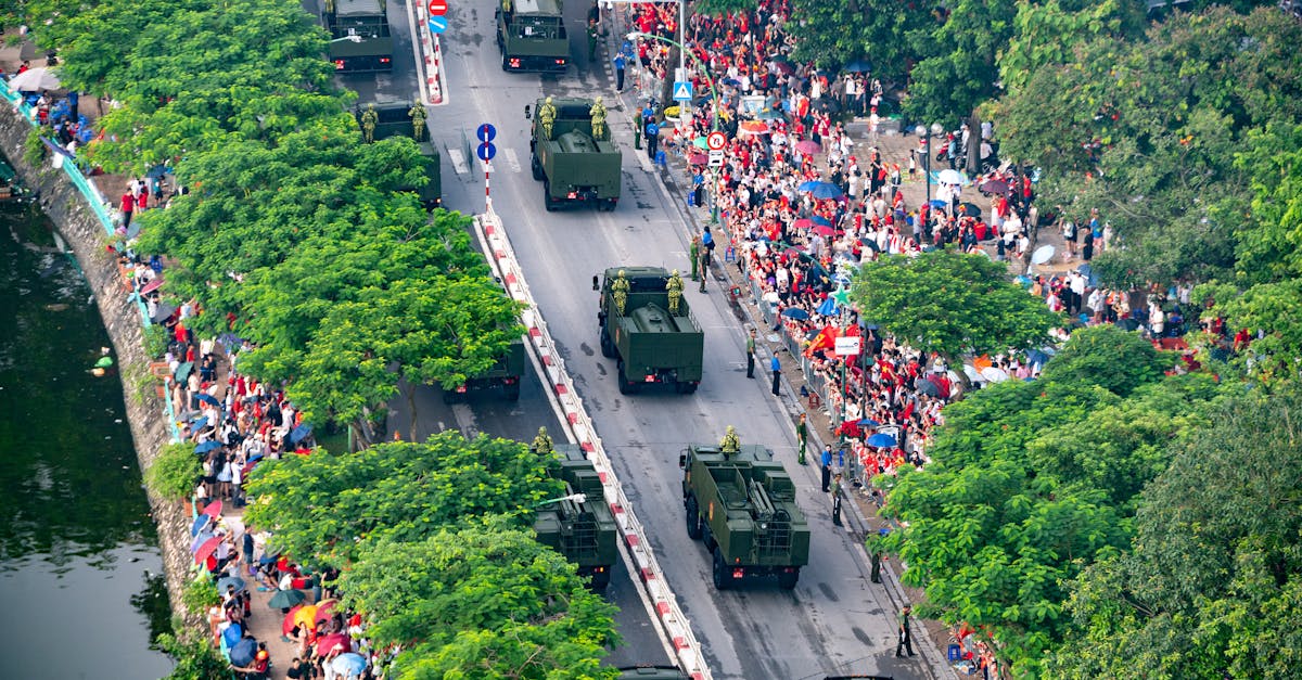 A vibrant aerial view of a military parade, surrounded by lush green trees and a large crowd, in a city street.