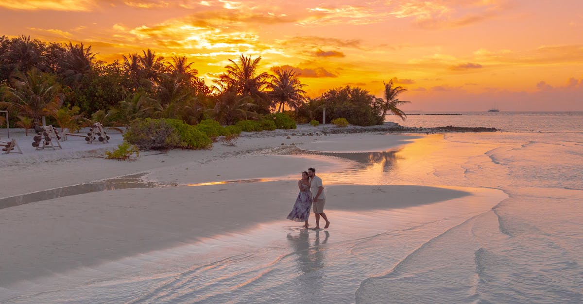 A couple enjoys a romantic stroll on a Maldivian beach during a vibrant sunset, surrounded by palm trees and serene waters.