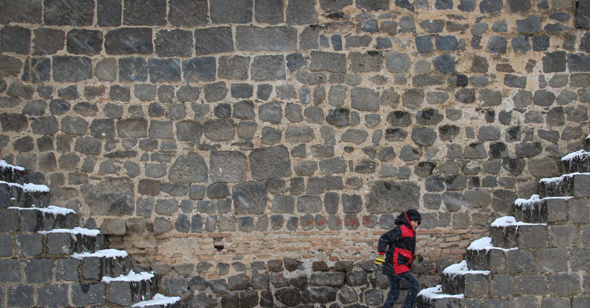 A child climbs ancient snow-dusted stone steps against a weathered brick wall.