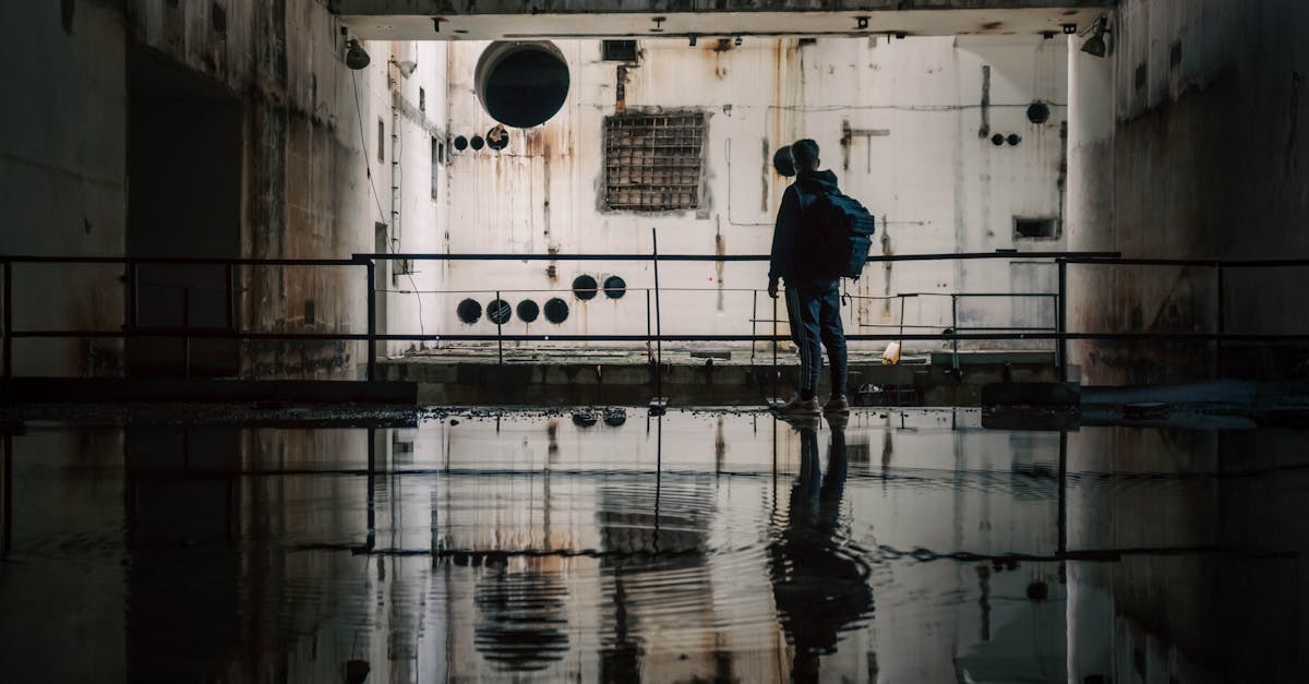 A person exploring a dark, abandoned industrial facility with water reflections.