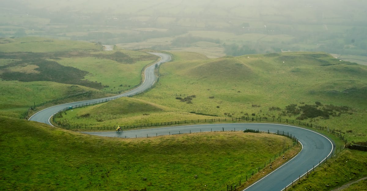 A solitary cyclist rides along a winding road through the lush, green hills of the English countryside.