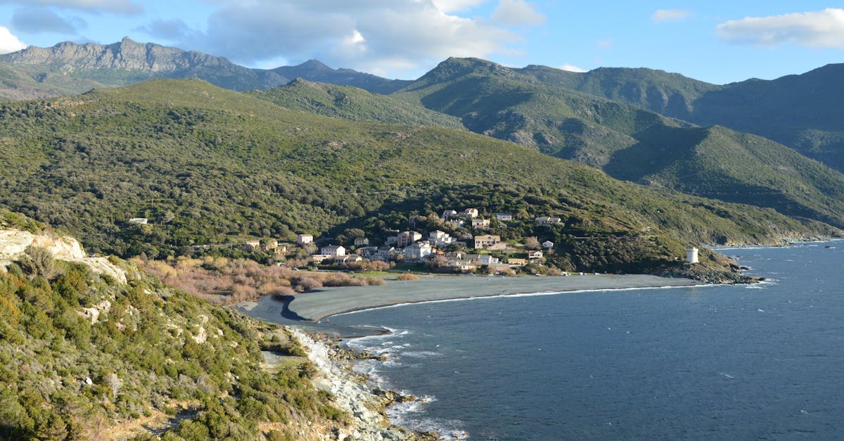Panoramic view of Ogliastro village on the Corsican coast surrounded by lush mountains and the Mediterranean Sea.