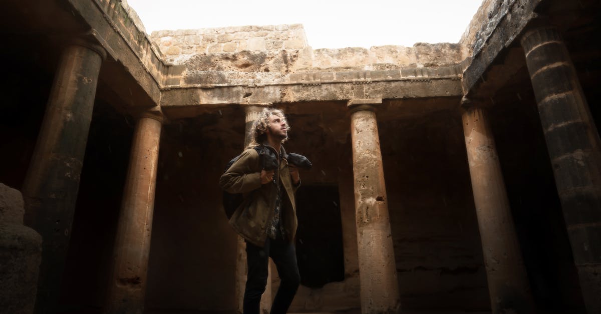 Man exploring ancient rock tombs with columns in Cyprus, highlighting historical architecture.