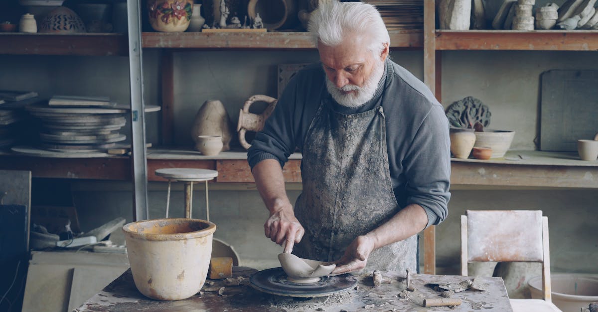 Senior potter skillfully shaping clay on a pottery wheel in a rustic studio setting.