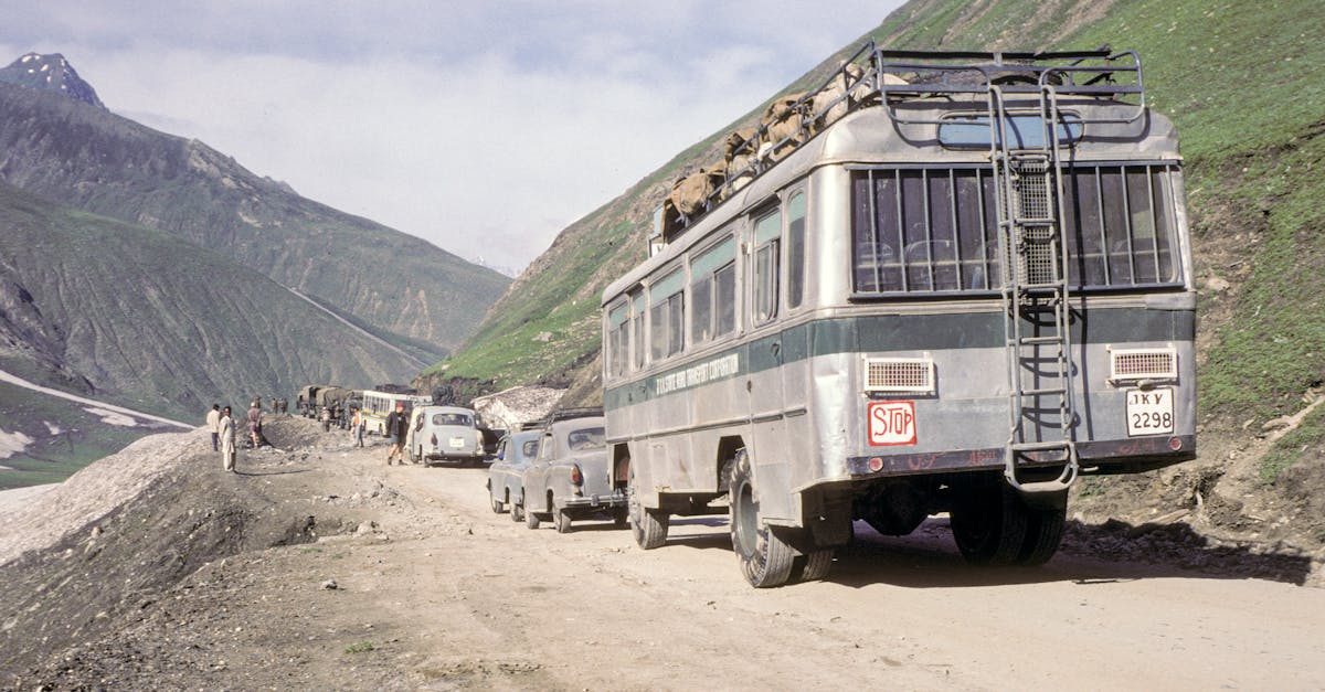 A scenic road journey in Ladakh, India with vintage vehicles traversing rugged mountain landscapes.