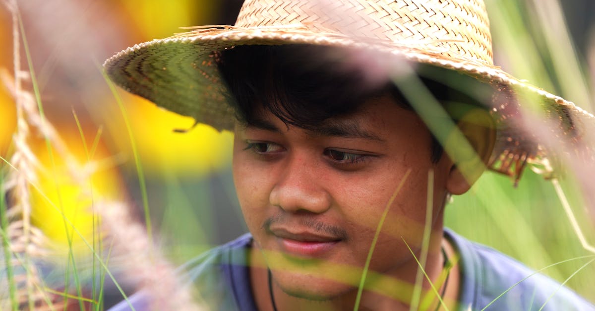 A young man with a straw hat amidst green grasses, showcasing rural lifestyle.