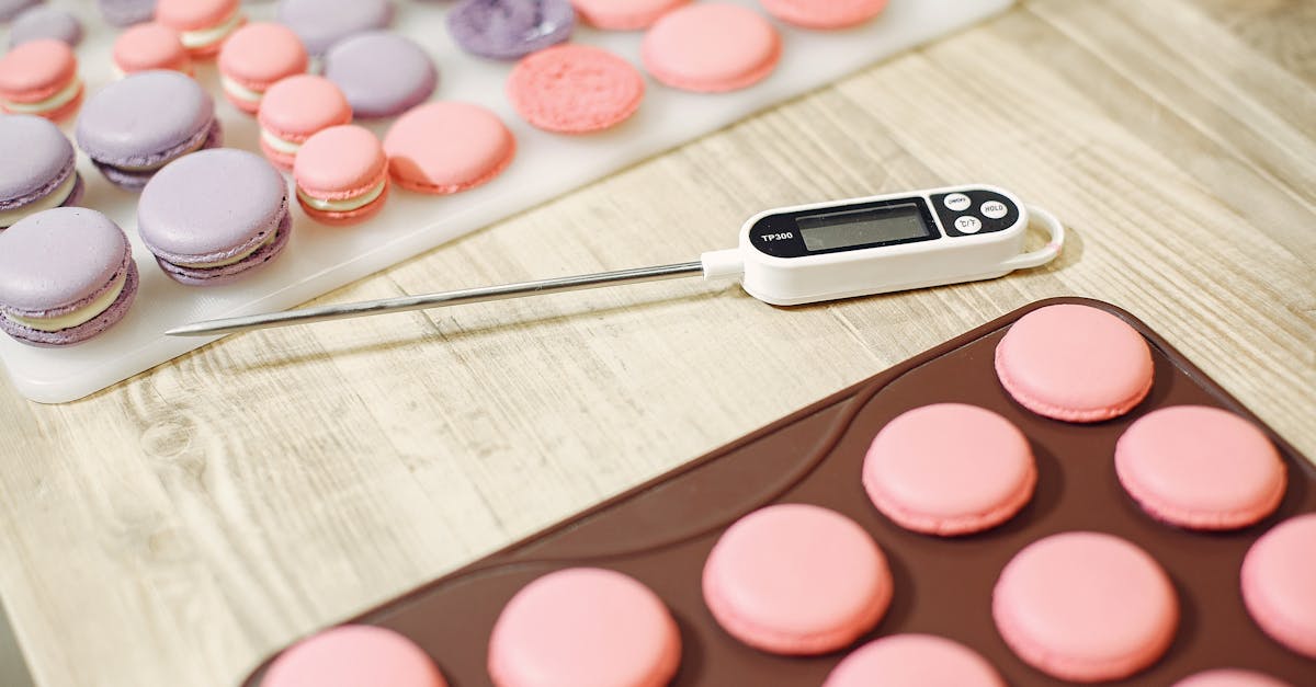 From above of colored macaroon shells placed on wooden table in pastry store with cooking thermometer