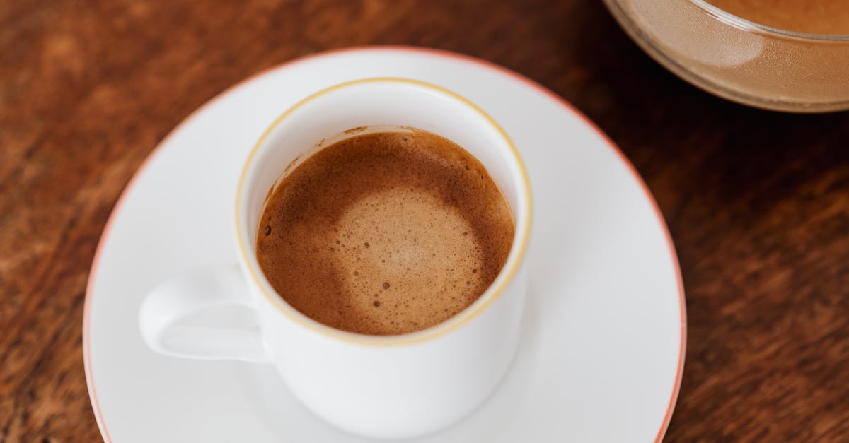 From above of cup of hot coffee with thin foam served on saucer standing on wooden table in cafe