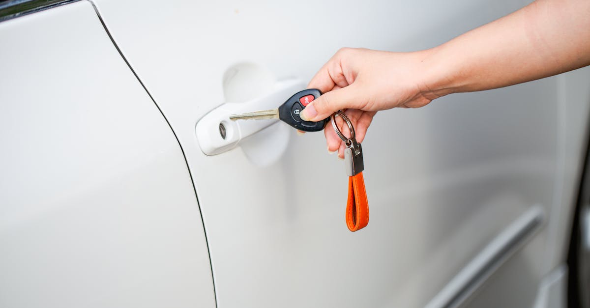 Close-up of a hand unlocking a white car door with a metal key and key fob.