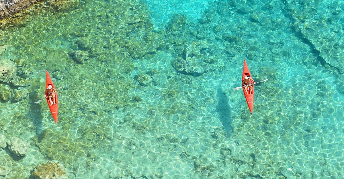 Aerial view of two kayakers paddling on crystal clear turquoise water near a rocky shore.