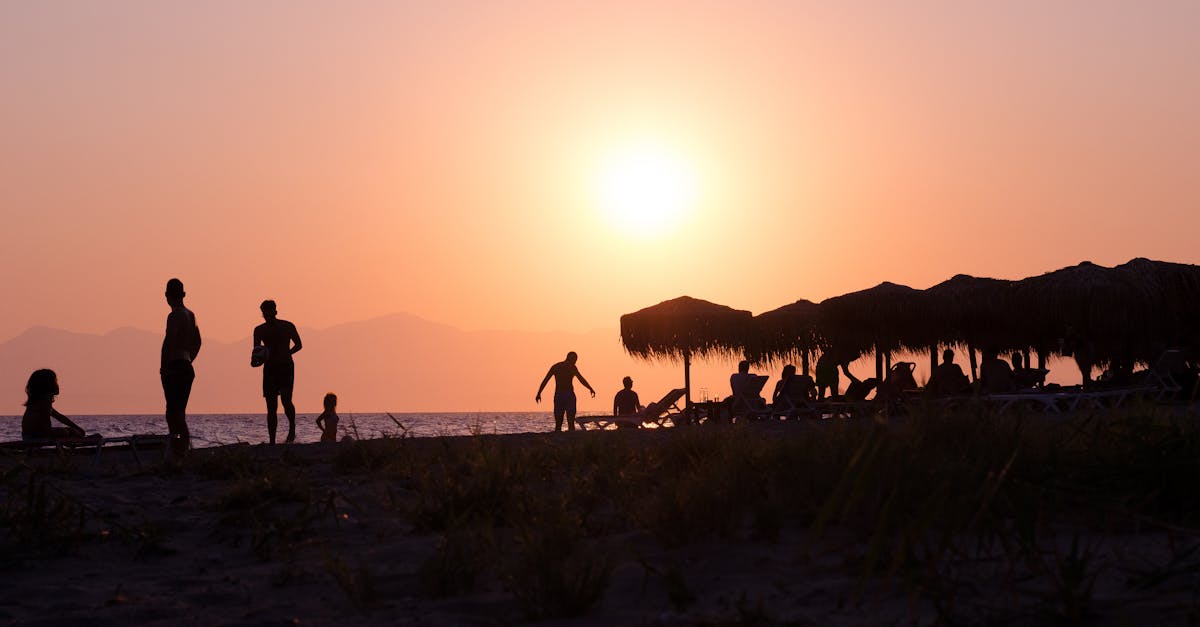 Peaceful beach scene in Greece with silhouetted figures and a vibrant sunset.