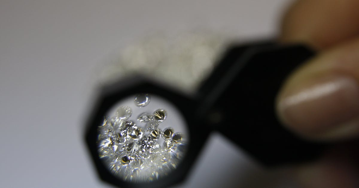 From above closeup of crop anonymous female jeweler with magnifying glass and diamonds in workshop
