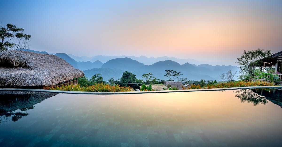 Clean water of pool located on tropical resort with wooden bungalows against silhouettes of mountain ridge on evening time in nature