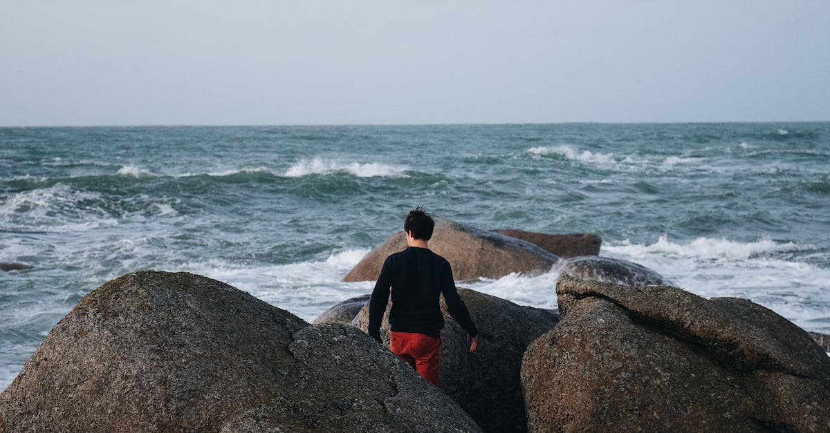 A man walks on rocky seashore in a serene coastal scene, capturing tranquil beach vibes.