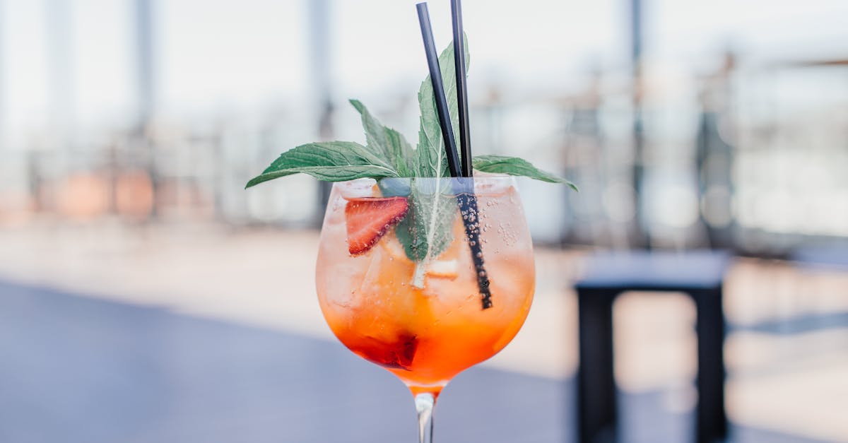 Close-up of a vibrant orange cocktail garnished with mint and strawberry, served in a glass with straws.