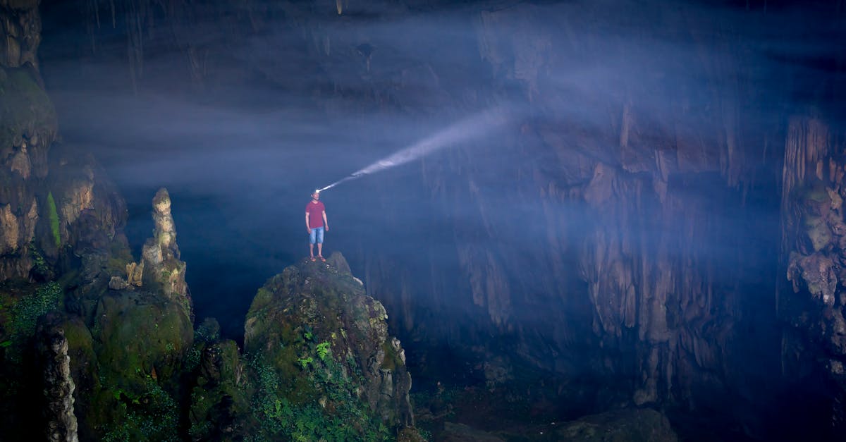 A person stands on a cave rock, illuminating the vast interior with a headlamp, showcasing adventure.