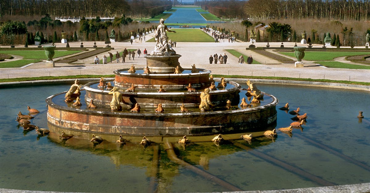 Classic fountain in the Gardens of Versailles surrounded by lush greenery and pathways.